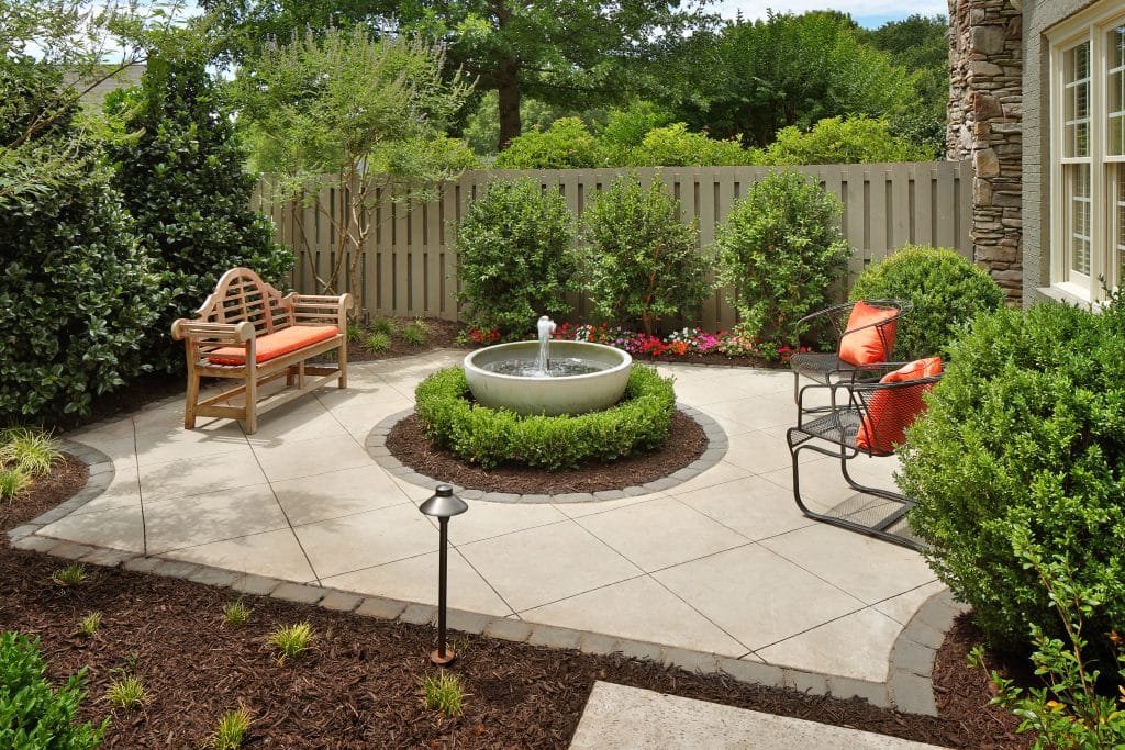 Compact backyard courtyard with circular fountain, manicured greenery, and cozy seating area.