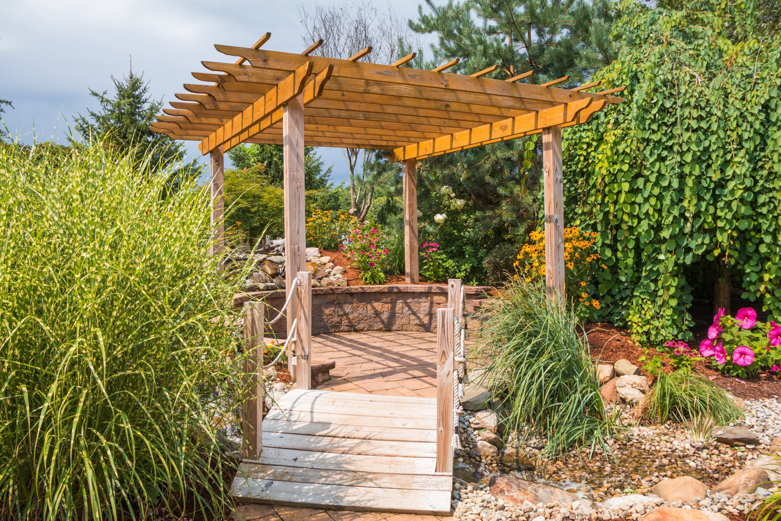 Wooden pergola over a garden path with vibrant flowers and a dry creek bed, adding structure and charm to a small backyard space.