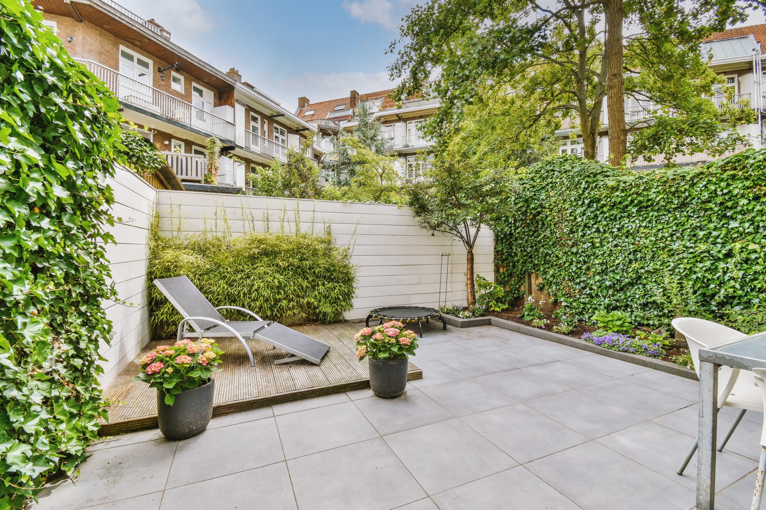 Small backyard patio with lounge chair, vertical greenery, potted plants, and privacy fencing.