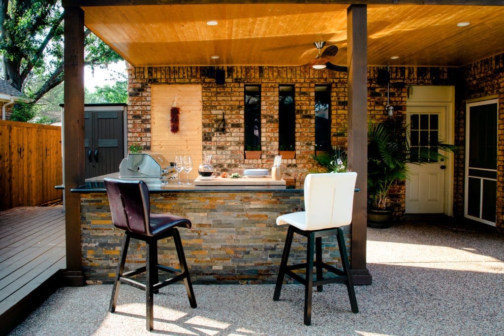 Covered patio with built-in outdoor kitchen and bar seating—stylish and functional low maintenance landscaping solution for year-round backyard use.